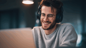A man young adult professional wearing headphones while watching an English TV show on a laptop he looks happy