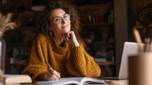 A woman who is motivated adult learner sitting at a cozy desk with a notebook, laptop, and grammar book open