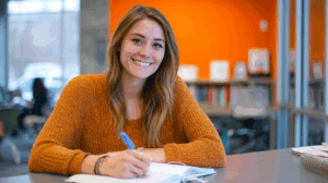 A young adult woman sitting at a desk with a notebook