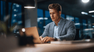 A young professional man sitting at a desk, typing on a laptop