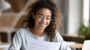 A confident young adult learner reviewing a finished grammar worksheet with all answers correct, smilin
