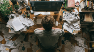 A person sitting at a desk with a computer and papers scattered around