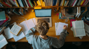 A student at a desk, putting away books and closing a laptop, having just completed their homework.