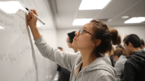 A student is pointing at a whiteboard while reviewing notes.