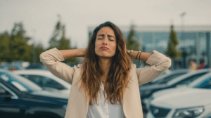 A woman standing outside a car dealership, shaking her head