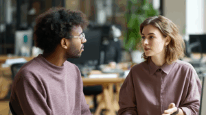 Two people having a conversation in an office setting. One person is speaking while the other listens, nodding in understanding.