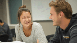 Two young adult learners facing each other smiling since they are playing game about English grammar