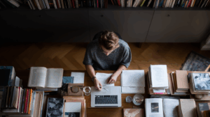 A person sitting at a desk, surrounded by books, notebooks, and a laptop, actively engaged in learning