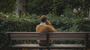 A person sitting on a park bench, holding a phone to their ear. 