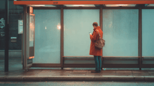 A person standing at a bus stop, looking at their phone