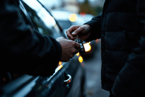 Someone holding a car key and standing next to a parked car, looking at it.