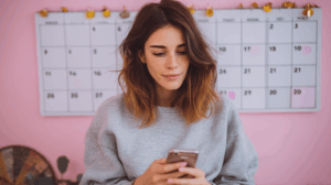 A girl texting on her phone with a calendar in the background