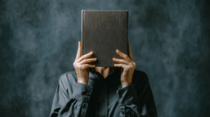 A person holding a closed book and shaking their head