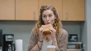 A woman in an office break room eating a sandwich