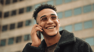 A young man outside on the phone, smiling or laughing while talking.